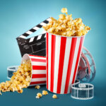 Elokuvamainoskuva, jossa popcorn-kippoja, filmirullaa ja klaffi.